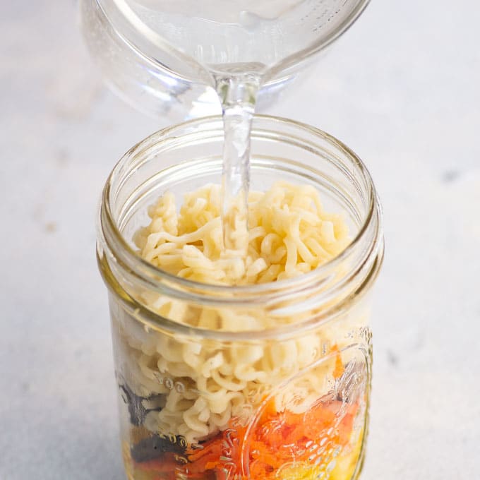 pouring water into a mason jar with noodles