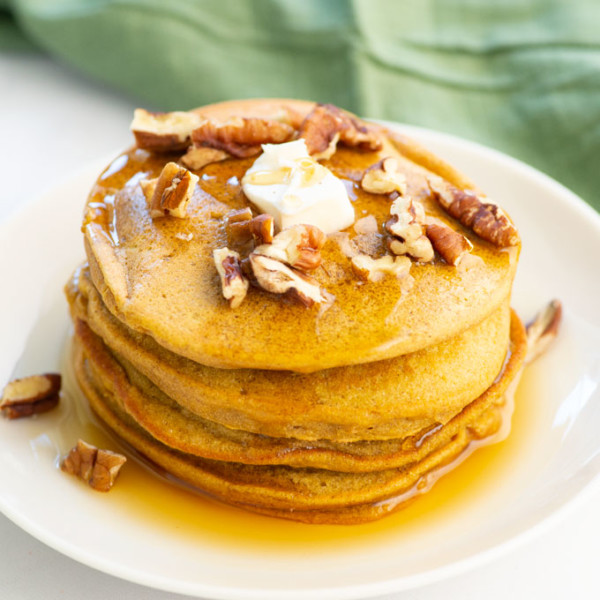 stack of vegan pumpkin pancakes with butter, maple syrup, and chopped pecans