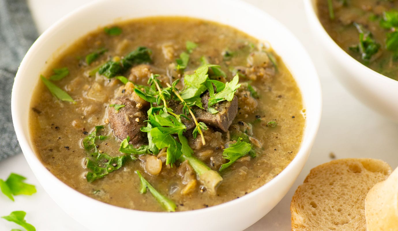 side angle of lentil leek soup with mushrooms and kale. topped with black pepper and parsley and served with bread.