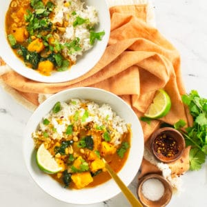 two bowls of vegan curry with lime, cilantro, chili flakes