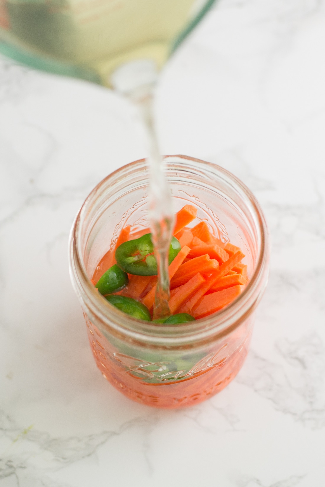 pouring water into mason jar with carrots and jalapenos
