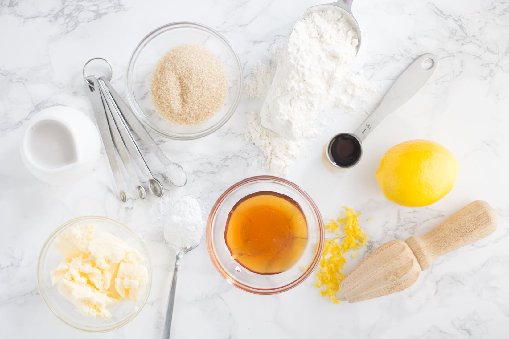 Lemon, vanilla extract, butter, flour, sugar on marble counter.