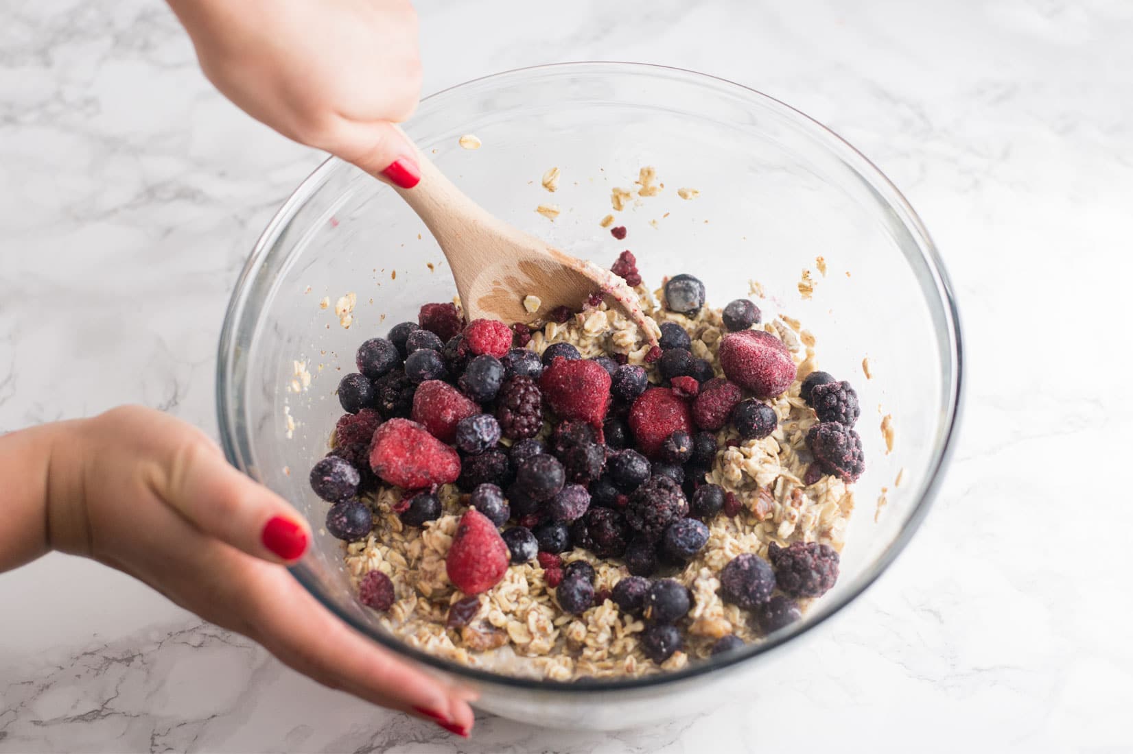 hands mixing bowl of berries and steel cut oats