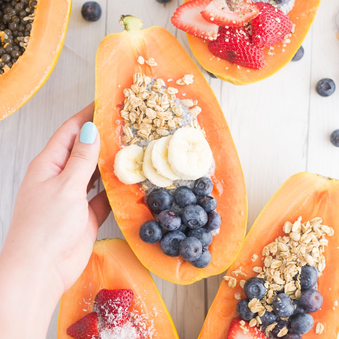 hand holding papaya boat topped with granola, bananas, and blueberries.