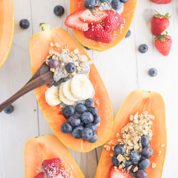 papaya boats with chia pudding, blueberries, strawberries, granola, on a white wood background