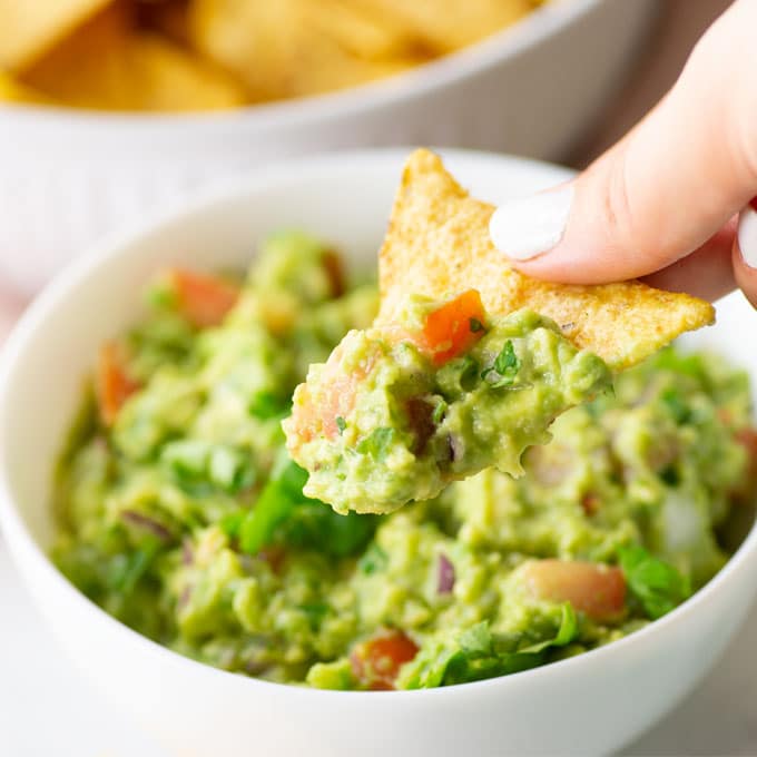 hand holding tortilla chip with guacamole
