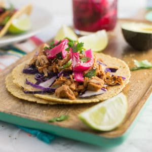 vegan jackfruit pulled pork tacos on wooden board with lime wedge and pickled red onions