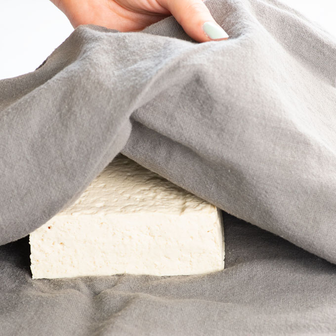hands wrapping a block of tofu to press it