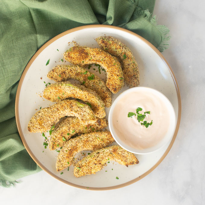 baked avocado fries on a plate with creamy sauce