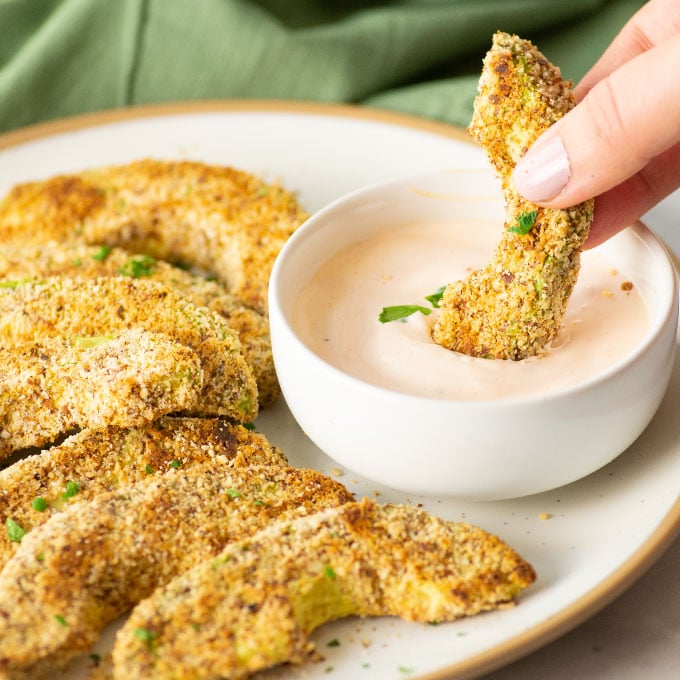 hand dipping baked avocado fries into sauce