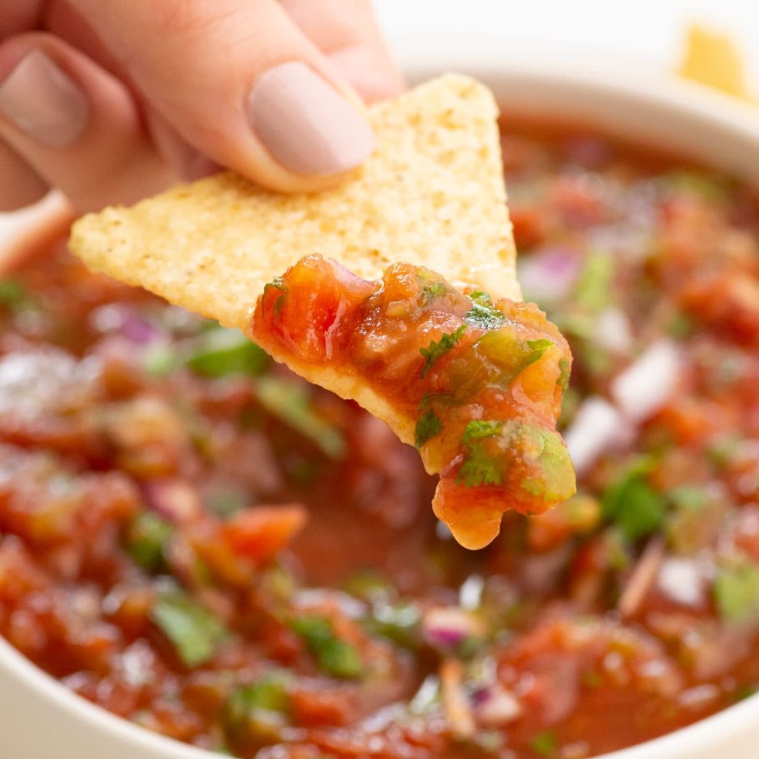 hand holding chip with salsa over bowl