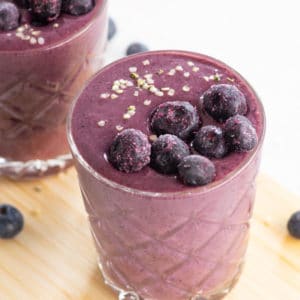 blueberry acai smoothie in glass topped with frozen blueberries and hemp seeds