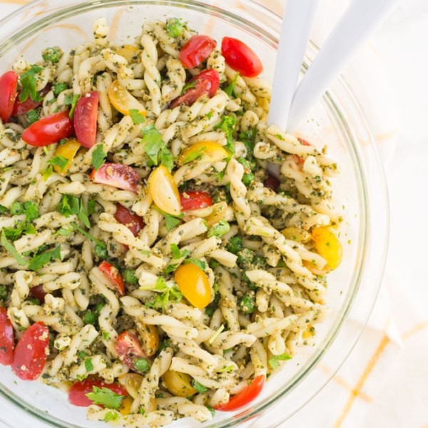 vegen pesto pasta salad with serving spoons on a yellow and white napkin