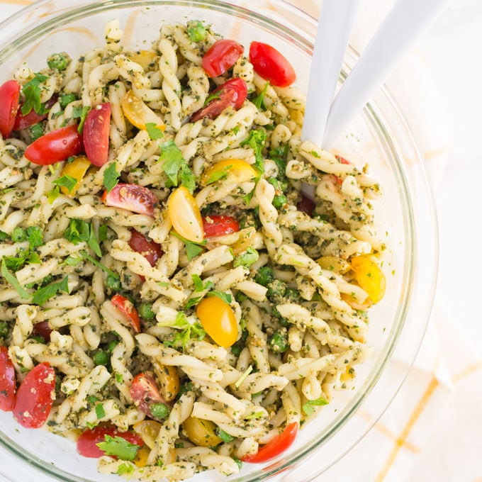 vegen pesto pasta salad with serving spoons on a yellow and white napkin