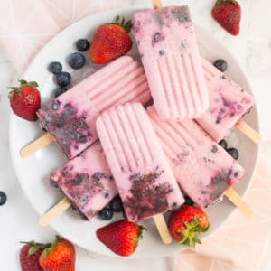 plate of yogurt berry popsicles with fresh blueberries and strawberries