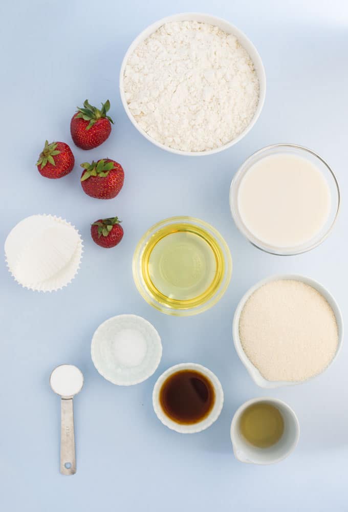 flour, sugar, oil, vanilla, baking soda, salt, almond milk, vinegar, and strawberries on blue background