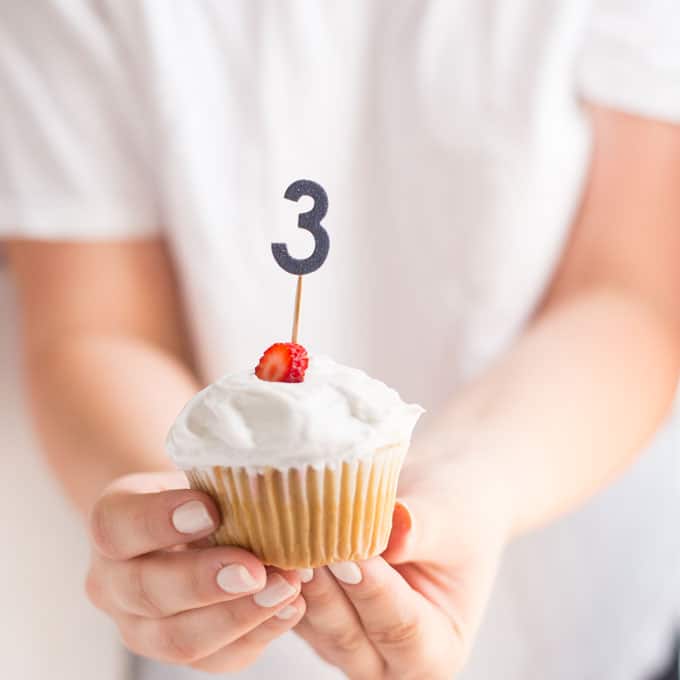 hands holding a vegan strawberry shortcake cupcake for a third birthday
