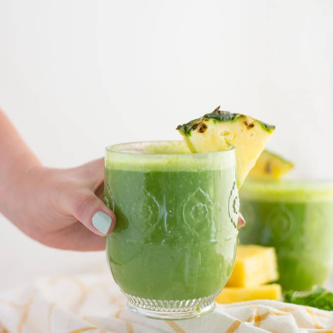 hand holding pineapple kale green smoothie with pineapple wedge