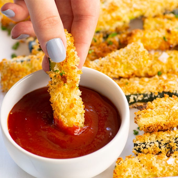 hand dipping zucchini fry into ketchup