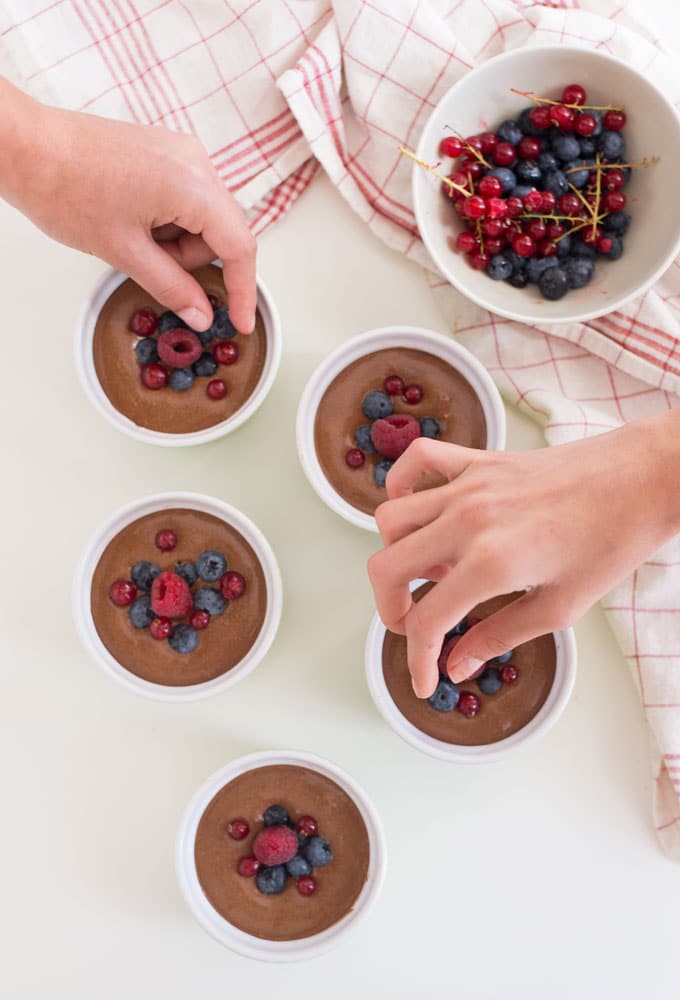 hands putting berries on chocolate mousse