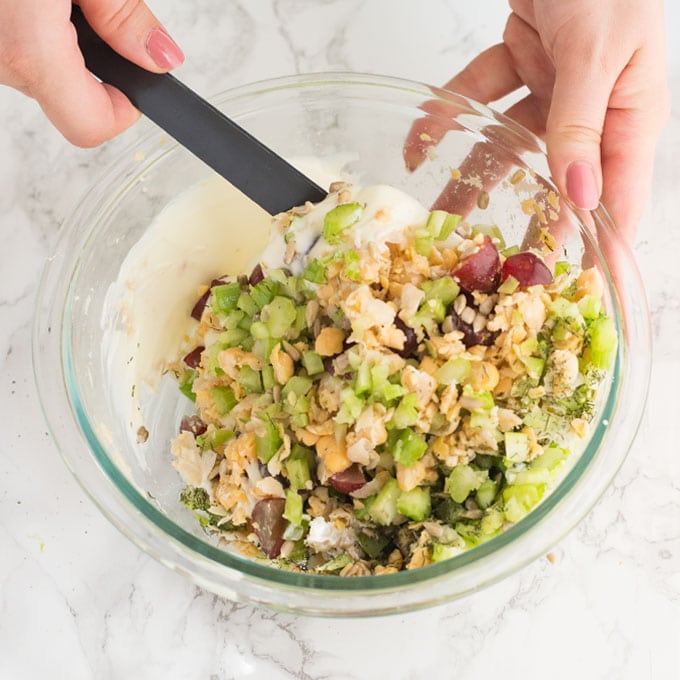 hands mixing vegan tuna salad in glass mixing bowl