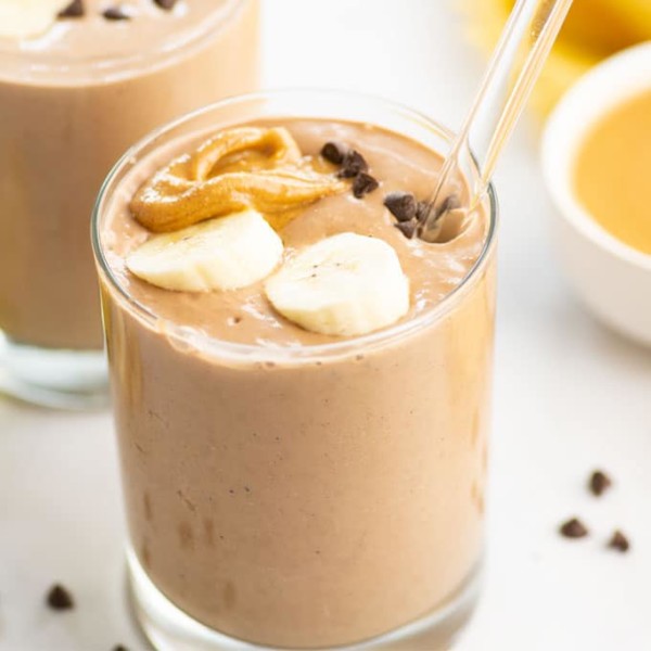 chocolate peanut butter banana smoothie with banana slices, chocolate chips and a glass straw
