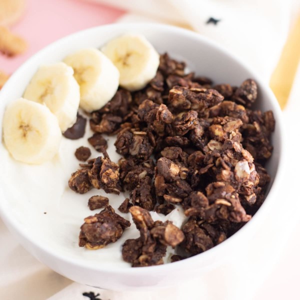 chocolate peanut butter granola in bowl with almond milk and banana slices