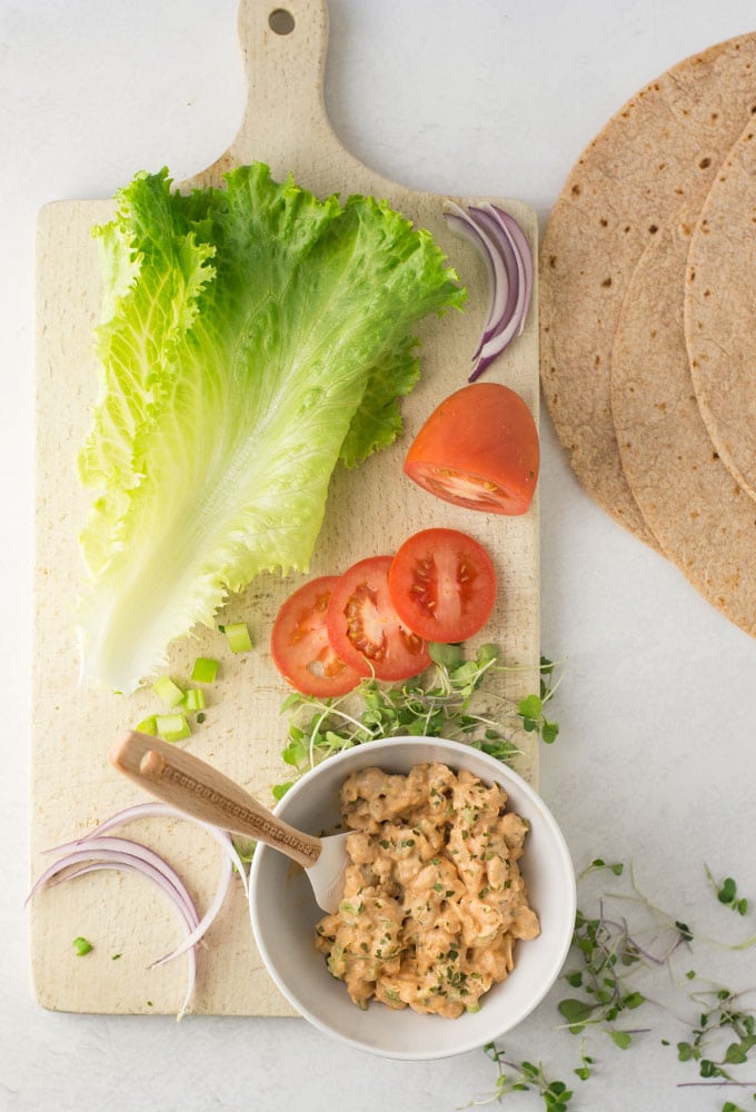 buffalo chickpea salad with lettuce, tomato, red onion, sprouts, and wraps on wood board