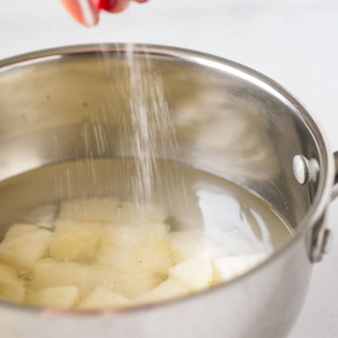 hand adding salt to pot of potatoes