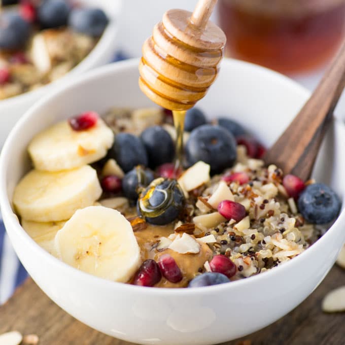 honey dripping on quinoa porridge with blueberries, bananas, pomegranate, and almonds