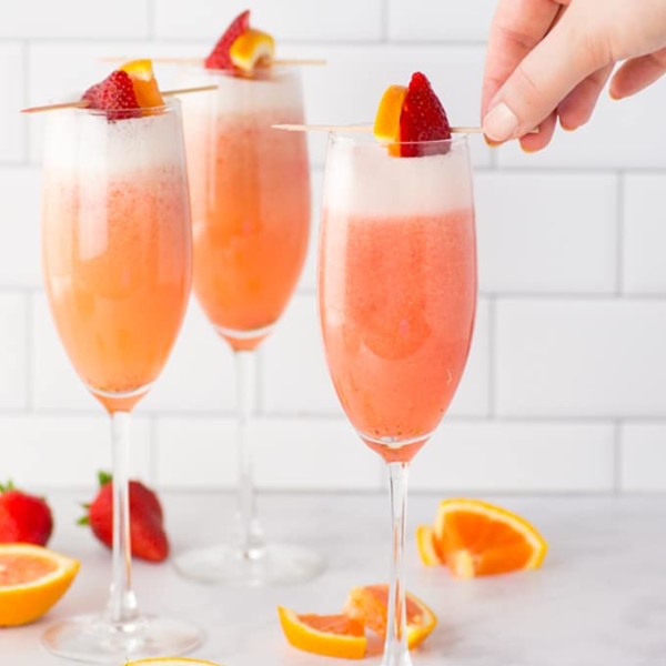 hand garnishing mimosas with strawberry and orange
