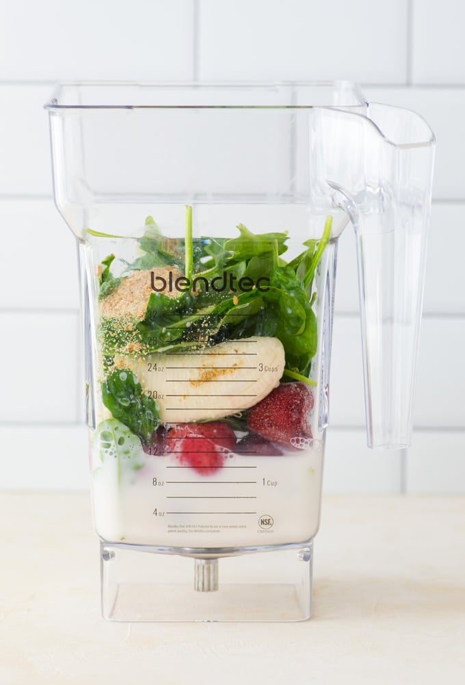 ingredients in blender for green smoothie with strawberries and bananas