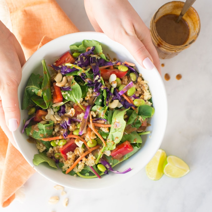 hands holding bowl of vegan thai quinoa salad with almond butter dressing and limes 