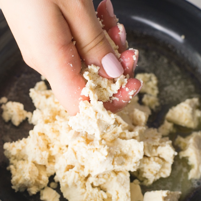 hands crumbling tofu over pan
