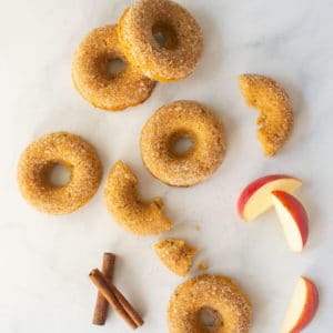 apple cider donuts with apple slices and cinnamon sticks on white background