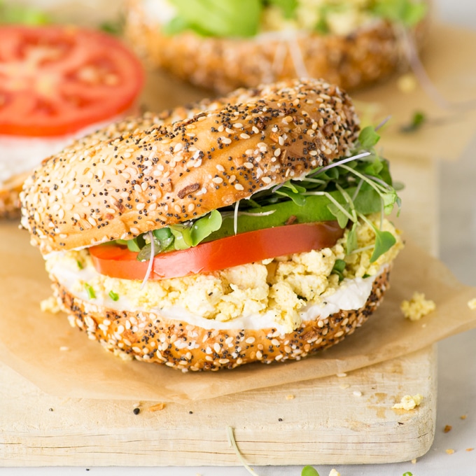 vegan breakfast sandwich on everything bagel with avocado, tomato, tofu scramble, sprouts