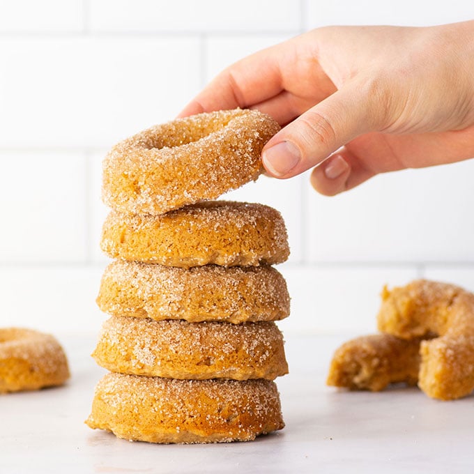 stack of vegan apple cider donuts with hand grabbing top donut.