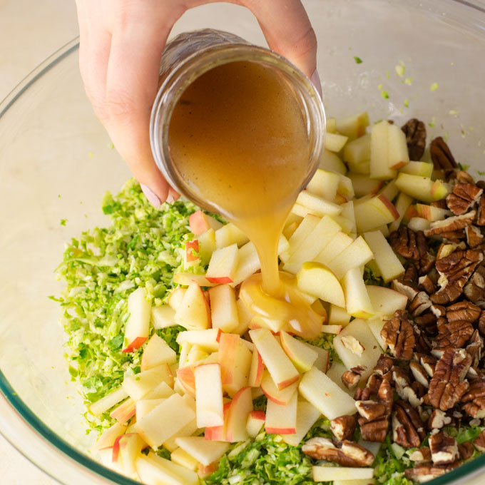 pouring dressing over apples, pecans, and shaved brussel sprouts