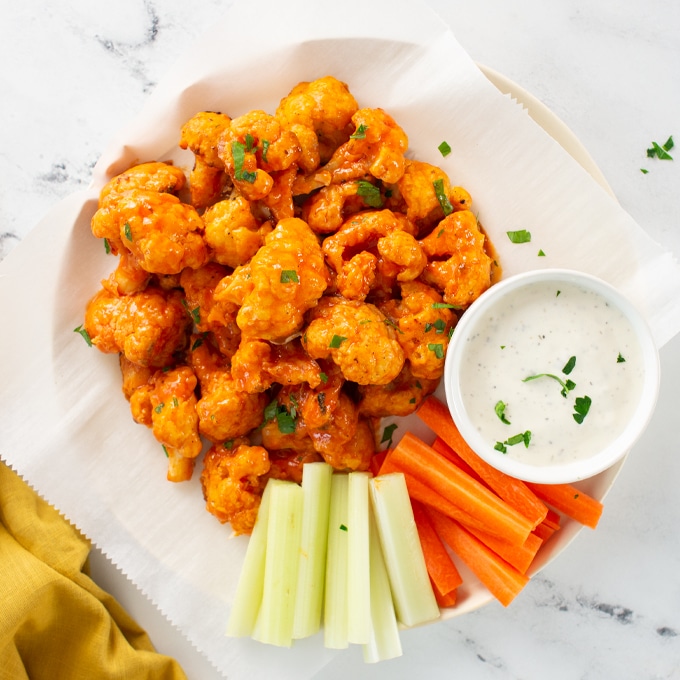 vegan buffalo cauliflower wings on plate with dip, celery, and carrots