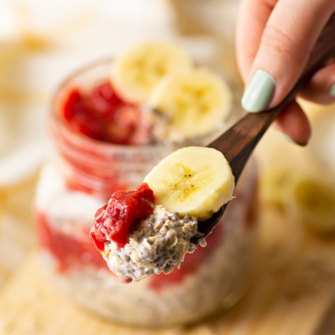 hand holding spoonful of overnight oats with strawberry and banana