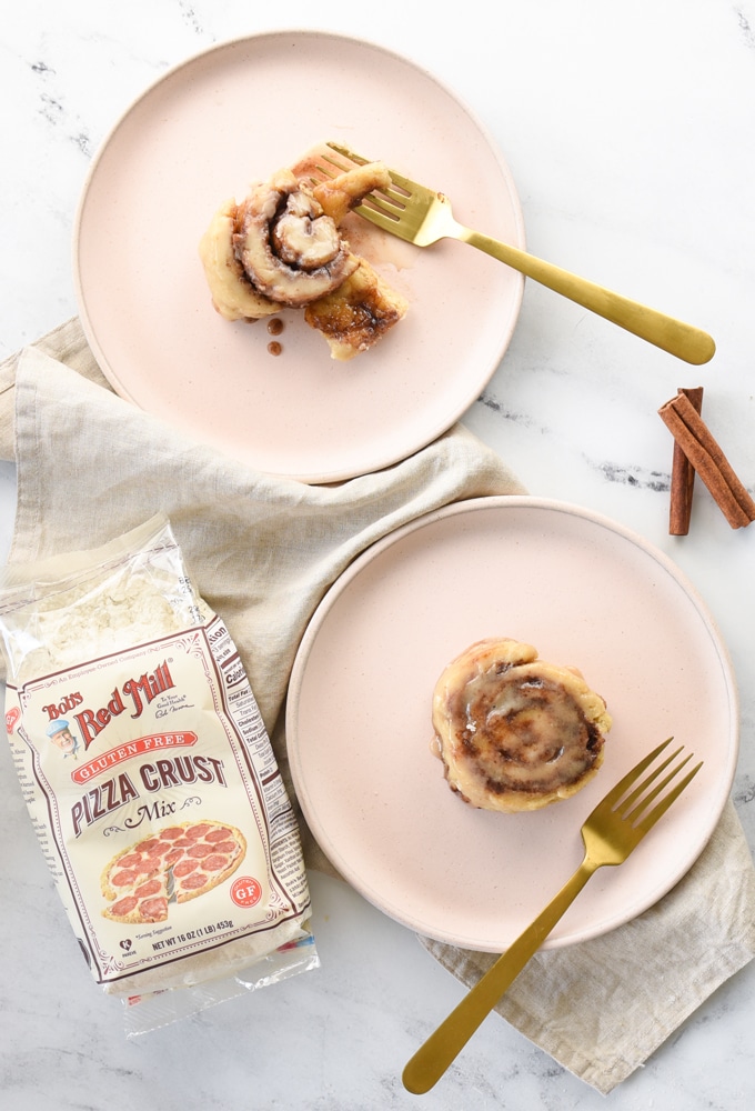 two cinnamon rolls on plates with Bobs Red Mill pizza dough mix