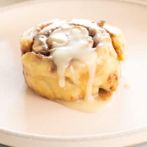 gluten free and vegan cinnamon roll on plate with icing dripping down side