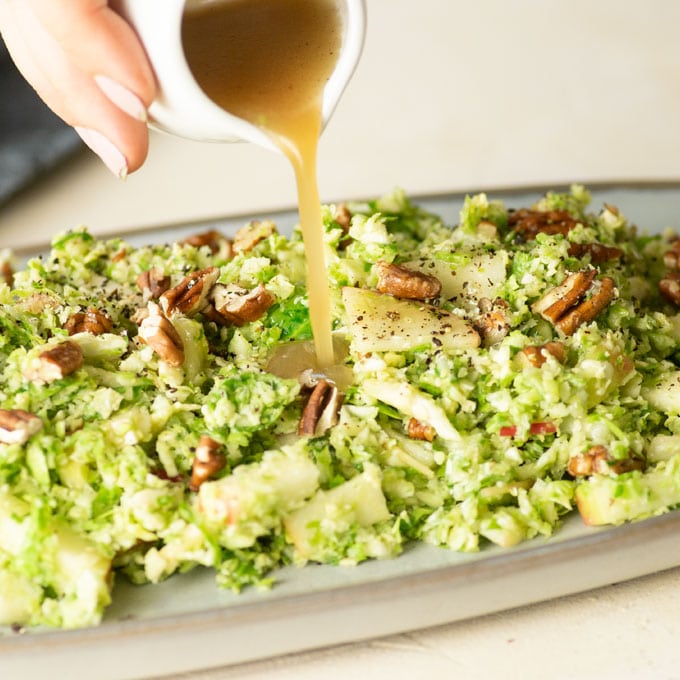 hand pouring dressing on shaved brussel sprout salad