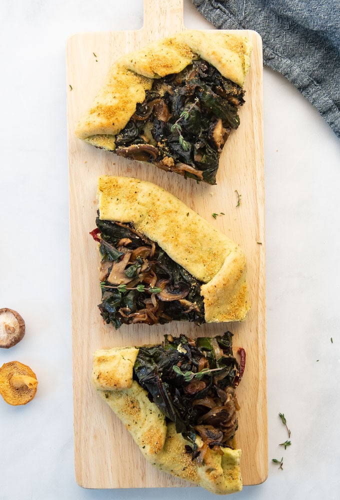three pieces of Swiss chard and wild mushroom galette on a board