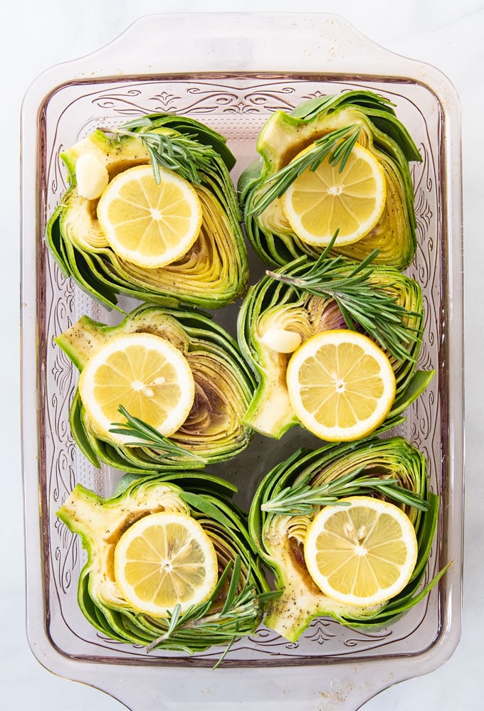 sliced artichokes in a baking dish with  herbs and lemon