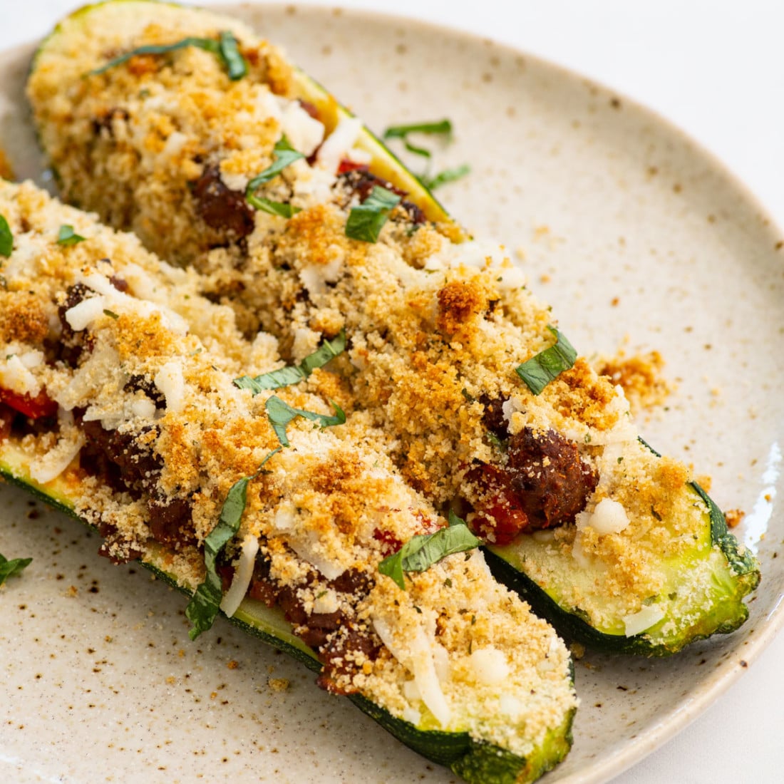 close up of vegan zucchini boats loaded with tomato sauce, cheese, and breadcrumbs