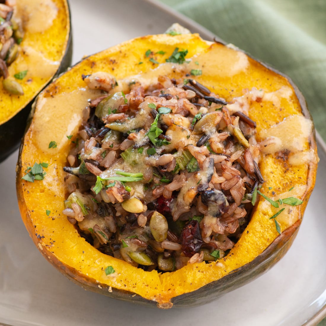 top up close view roasted acorn squash stuffed with rice, pepitas, cranberries and walnuts mixture, drizzle with tahini maple sauce