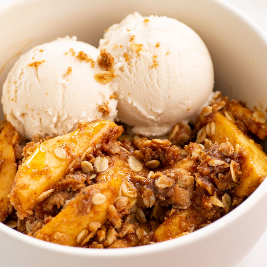 close view of white bowl with apple crisp and two scoops of vegan vanilla ice cream
